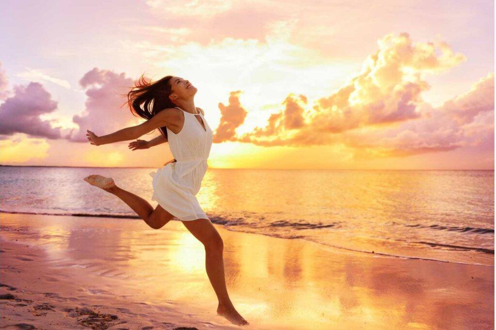 Femme qui danse librement sur une plage et en ressent les bienfaits